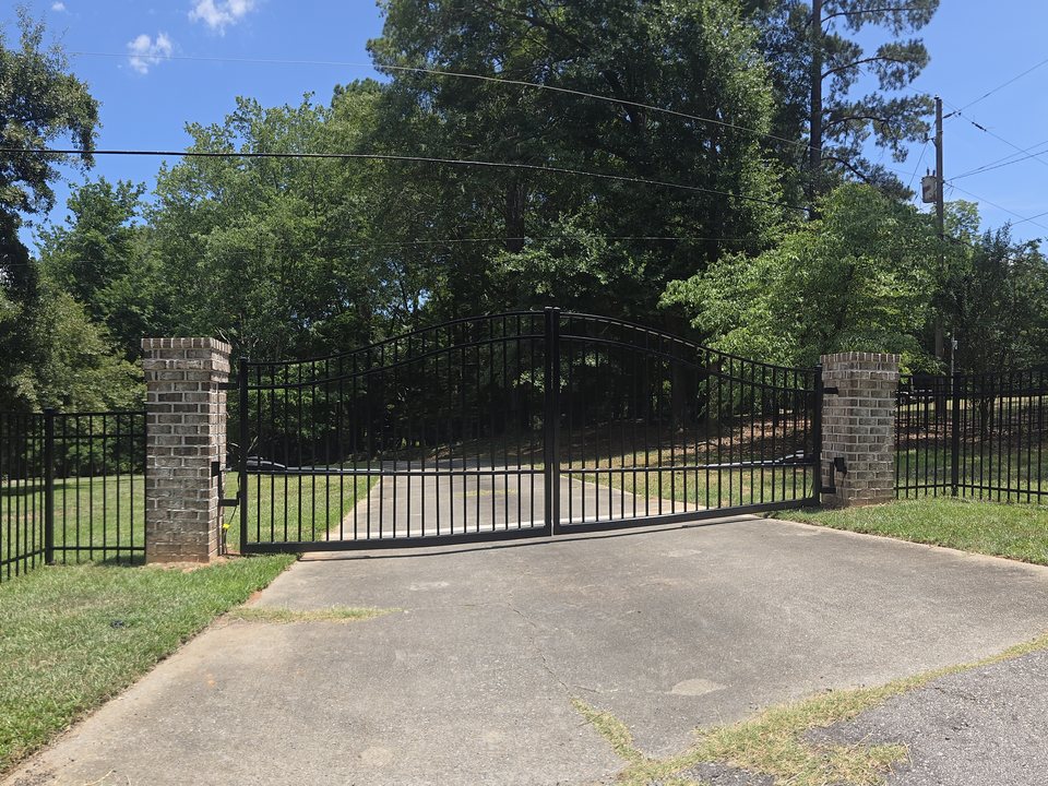 Black aluminum arched double drive gate between brick pillars at a driveway entrance in the Midlands of SC