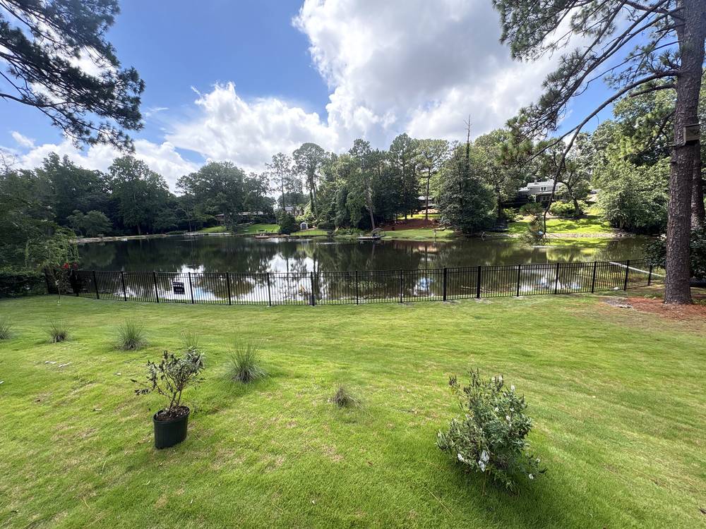 Black aluminum fence across the far side of a green lawn above a pond in the Midlands of South Carolina