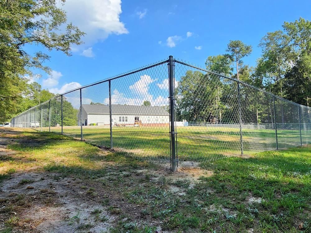 Galvanized chain link fence running to a corner post across a yard in the Midlands of South Carolina