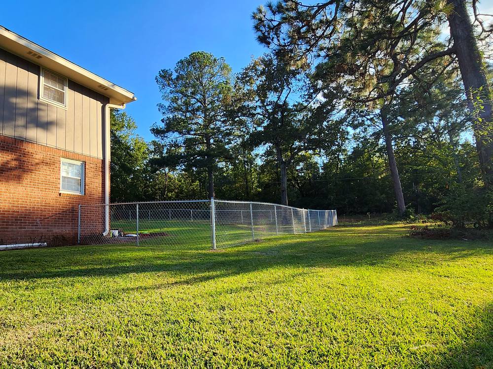 Galvanized chain link fence around a green lawn beside a brick home in the Midlands of South Carolina