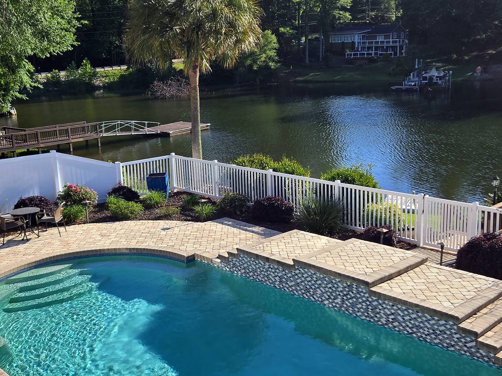 White vinyl pool fence along a paver patio beside a lake in Irmo, SC