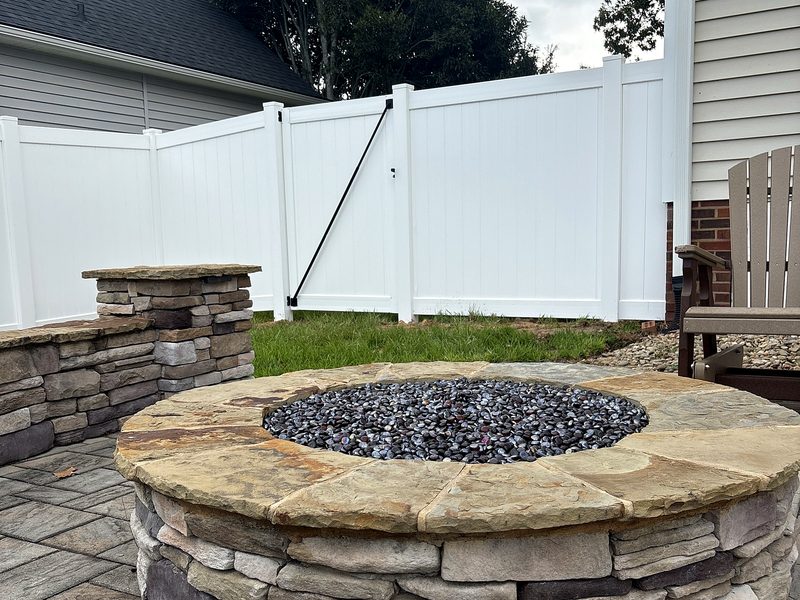 White vinyl privacy fence behind a stone fire pit patio in Lexington, SC